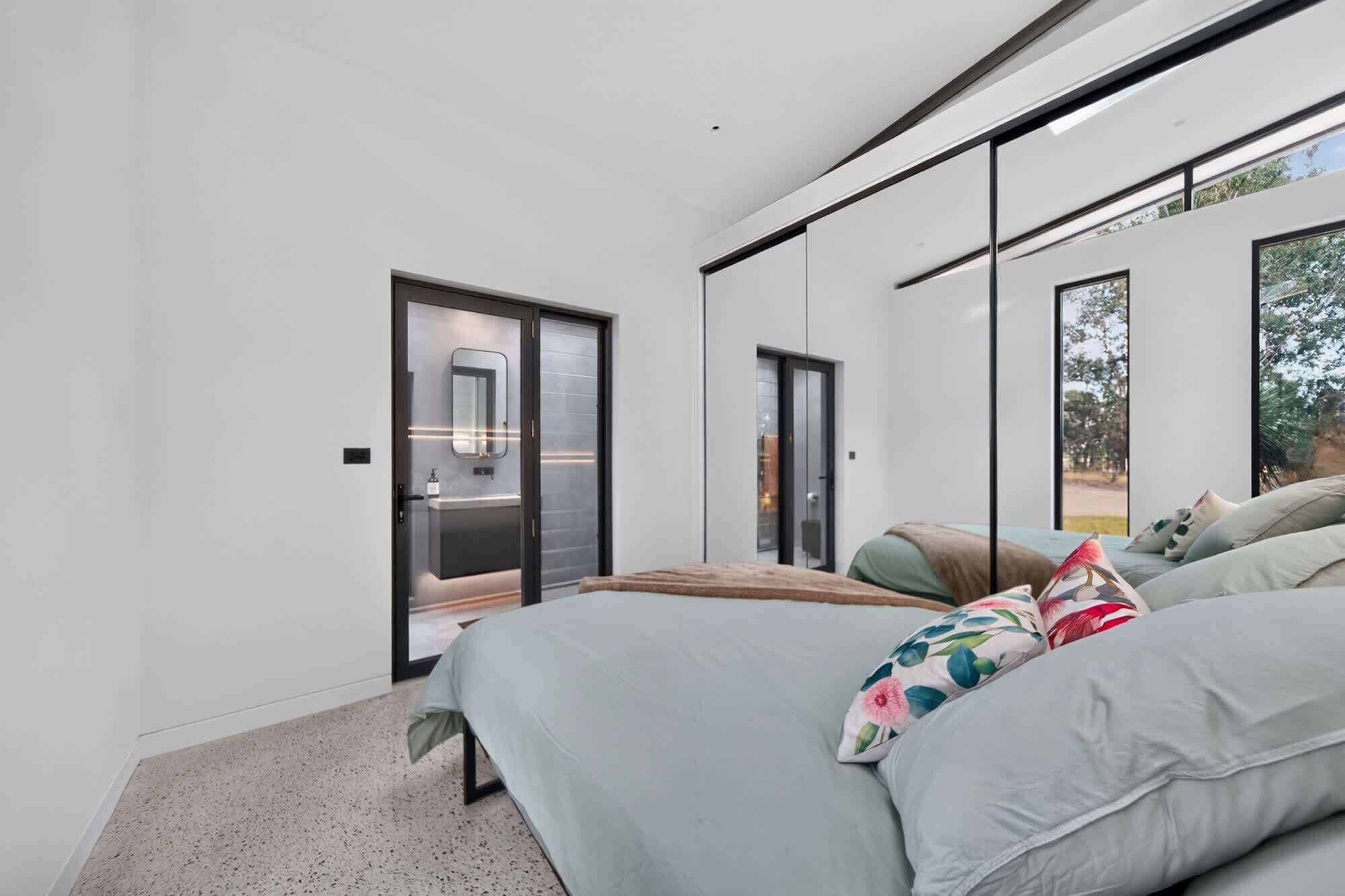 Een moderne slaapkamer met een bed, een groot raam en een schuifdeur naar een badkamer.