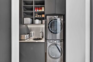A compact kitchen with a built-in washer and dryer, a coffee maker, and a small countertop with a toaster. - Luxury Nature-Surrounded Estate House With Pool (Theresa Park)