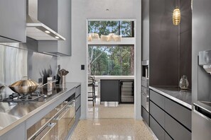Una cocina moderna con electrodomésticos de acero inoxidable, estufa a gas y un amplio ventanal con vistas a árboles.
