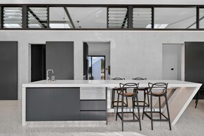 A modern kitchen with a central island, bar stools, and a view of the outdoors. - Luxury Nature-Surrounded Estate House With Pool (Theresa Park)