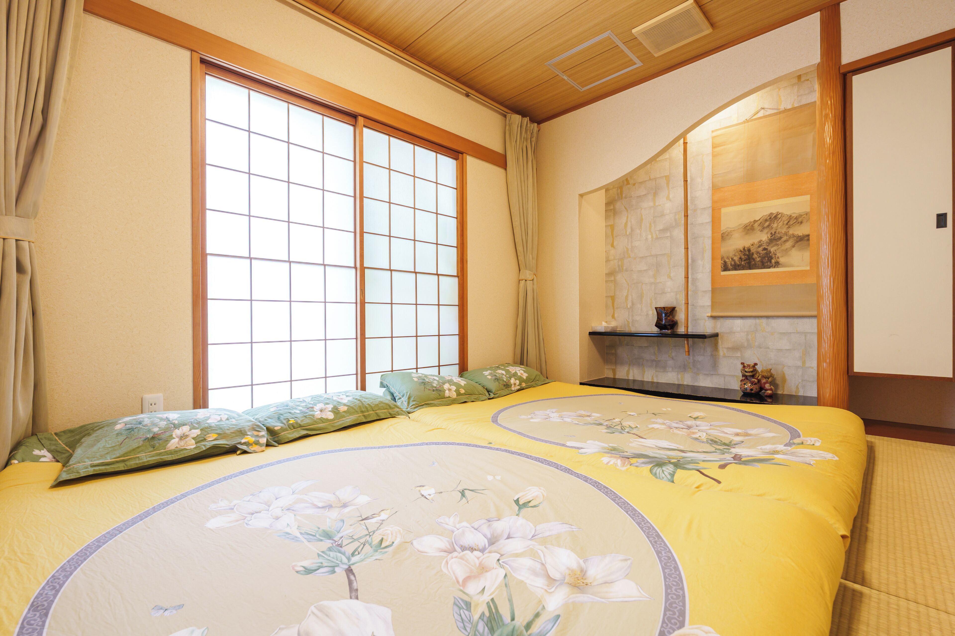A traditional Japanese-style room with tatami flooring, a shoji screen, and a bed with floral bedding.