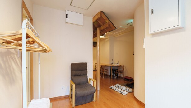 A room with a wooden floor, a chair, a table with chairs, and a hanging clothes rack.