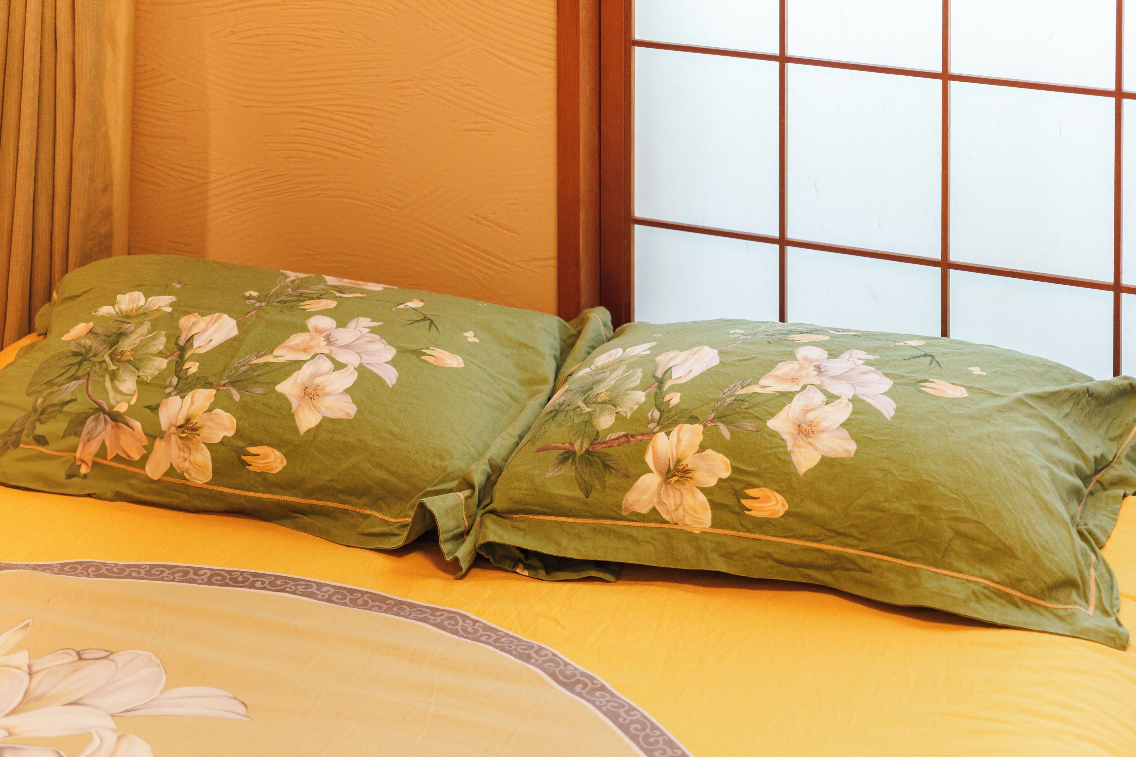 A bed with green floral bedding and a window with a grid pattern.