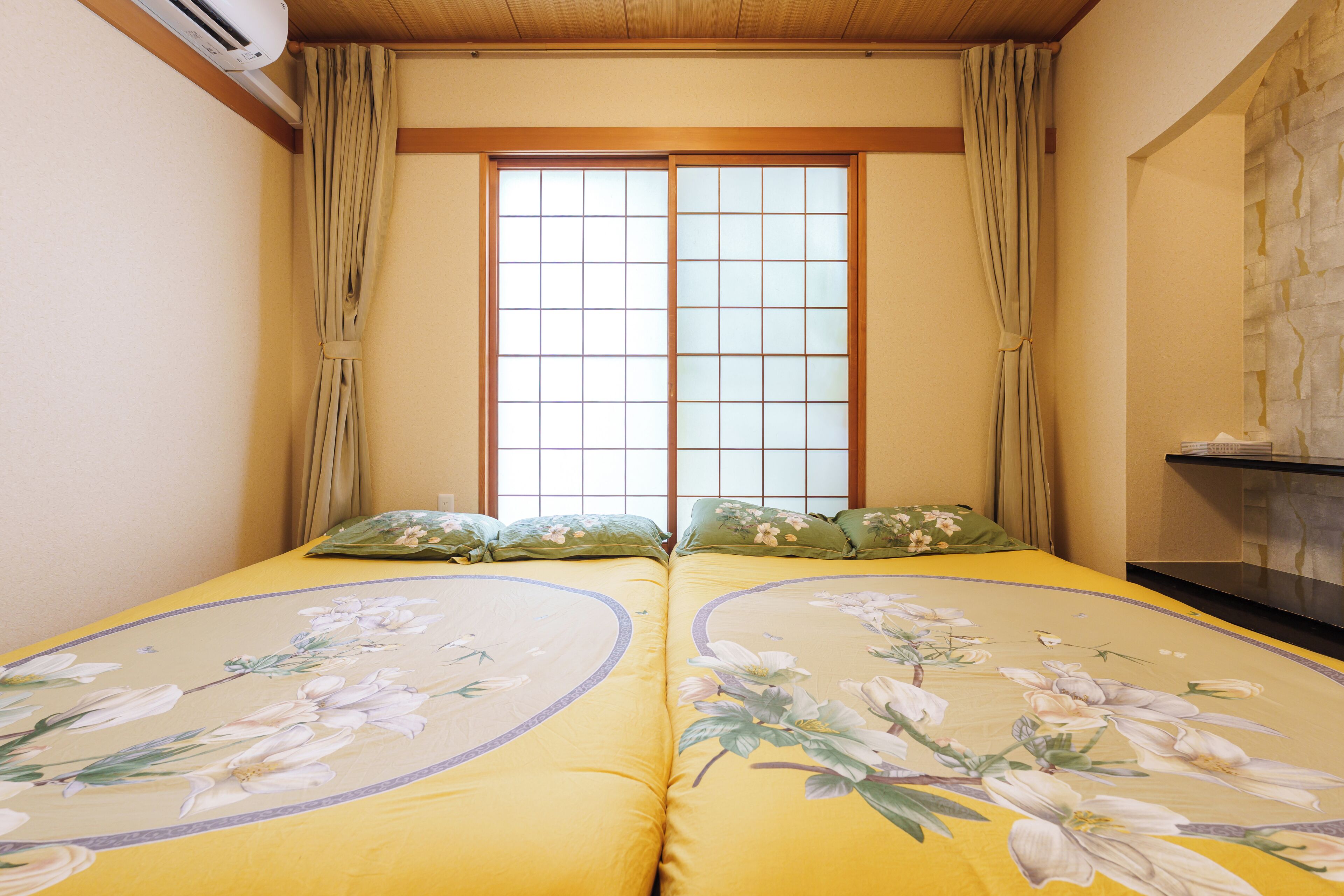 A room with a bed featuring floral bedding, a window with a grid pattern, and curtains.