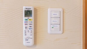 Termostato y panel de control fijados a la pared, con etiquetas en japonés que indican la temperatura y funciones de la habitación.