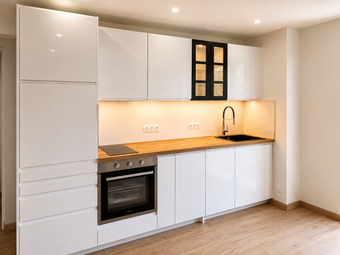 A modern kitchen with white cabinetry, a wooden countertop, a built-in oven, a sink, and a black cabinet above the countertop.