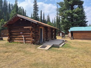 A rustic log cabin with a door, a sign indicating 'No Parking,' and a small outdoor seating area.