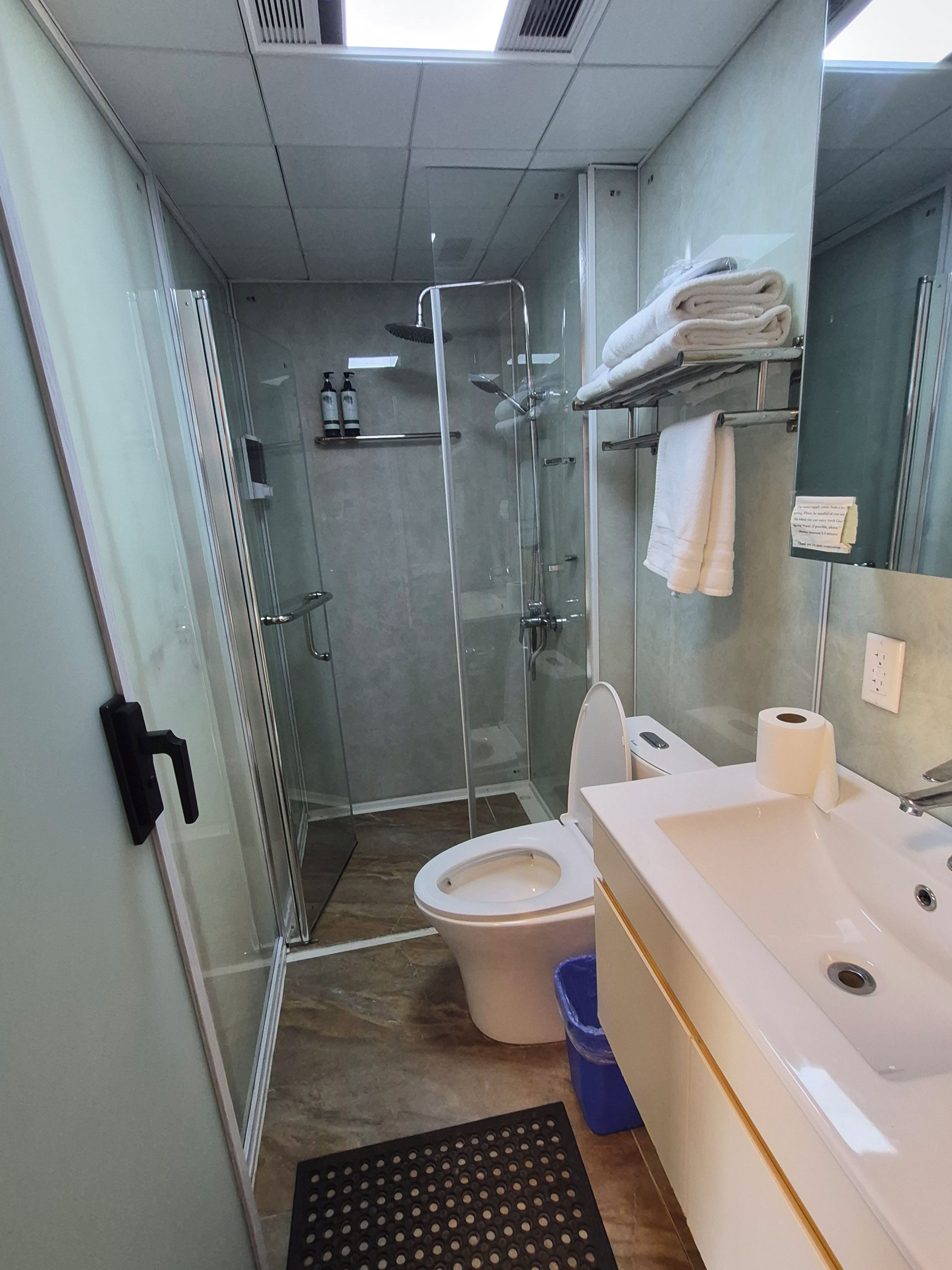 Un baño moderno con ducha envuelta en cristal, inodoro blanco y lavamanos con espejo.