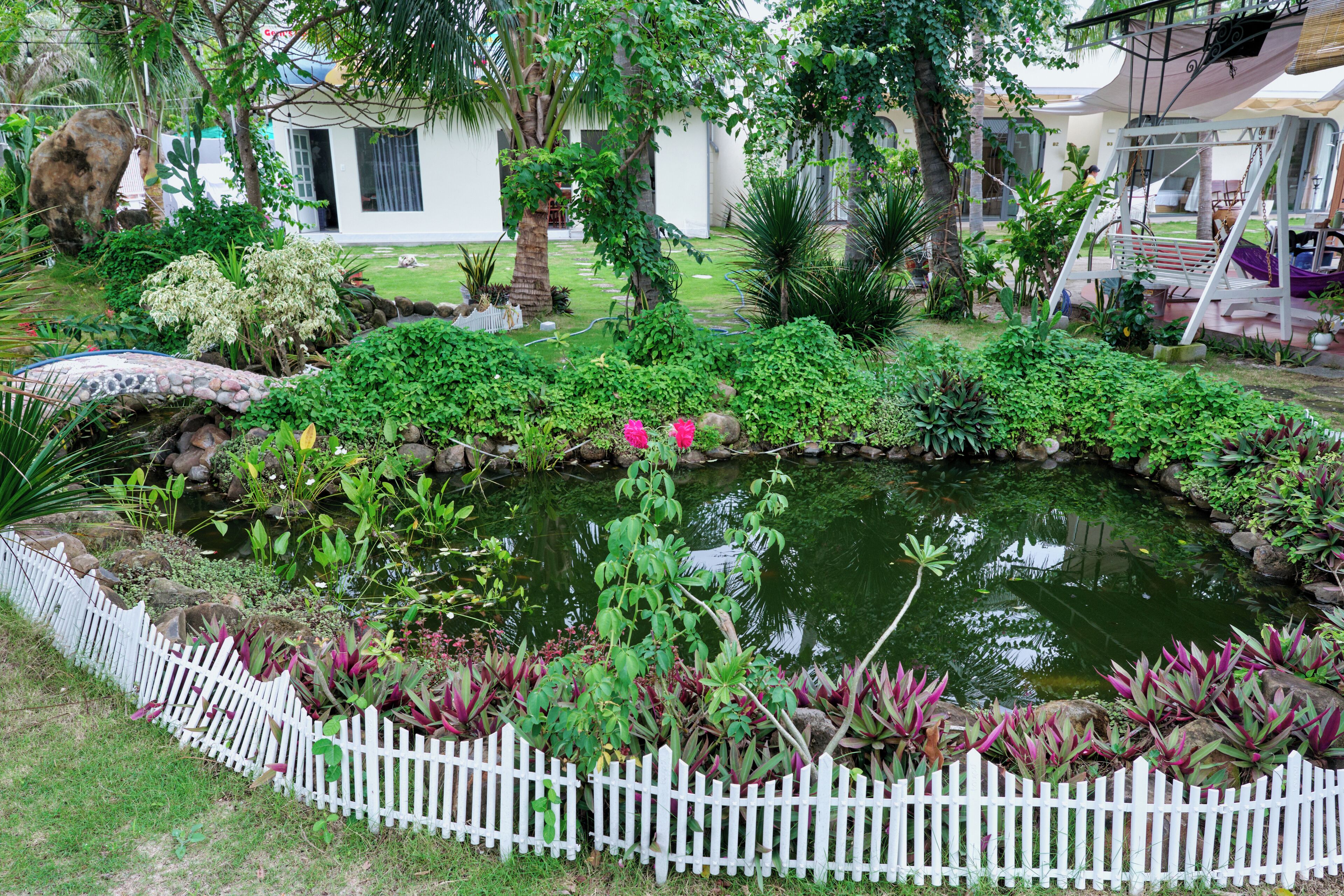 A garden with a pond, white picket fence, and various plants.