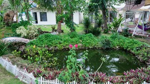 Un jardin avec un bassin, une clôture en bois peinte en blanc et diverses plantes.