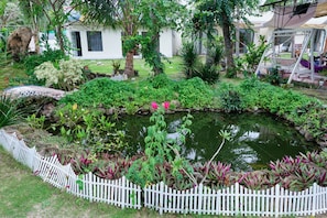 A garden with a pond, white picket fence, and various plants. - Gem's House (Mui Ne)