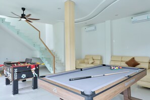 A modern living room with a pool table, a foosball table, a sofa, and a staircase. - Gem's House (Mui Ne)