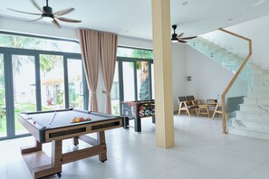 A modern indoor space with a pool table, a foosball table, and a staircase with glass railings. - Gem's House (Mui Ne)