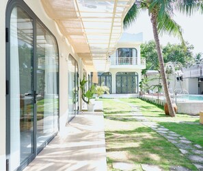 A modern hotel with a covered walkway, a pool area, and lush greenery. - Gem's House (Mui Ne)
