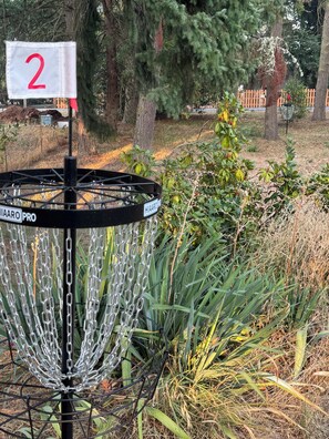 En discgolfkorg med en vit skylt som visar siffran 2, omgiven av grönska och träd.