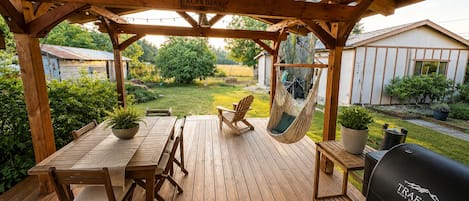 A wooden deck with a table and chairs, a hanging chair, and a grill.