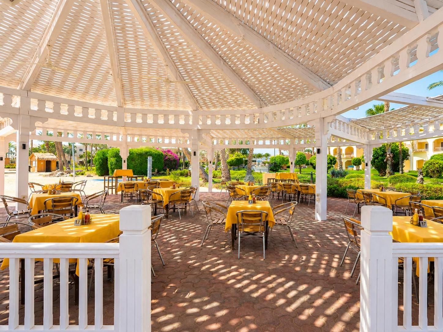 An outdoor patio with tables and chairs, covered by a white pergola structure.