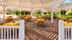 En udendørs terrasse med borde og stole, overdækket af en hvid pergola.
