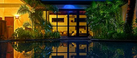A nighttime view of a hotel with a swimming pool, palm trees, and a starry sky.