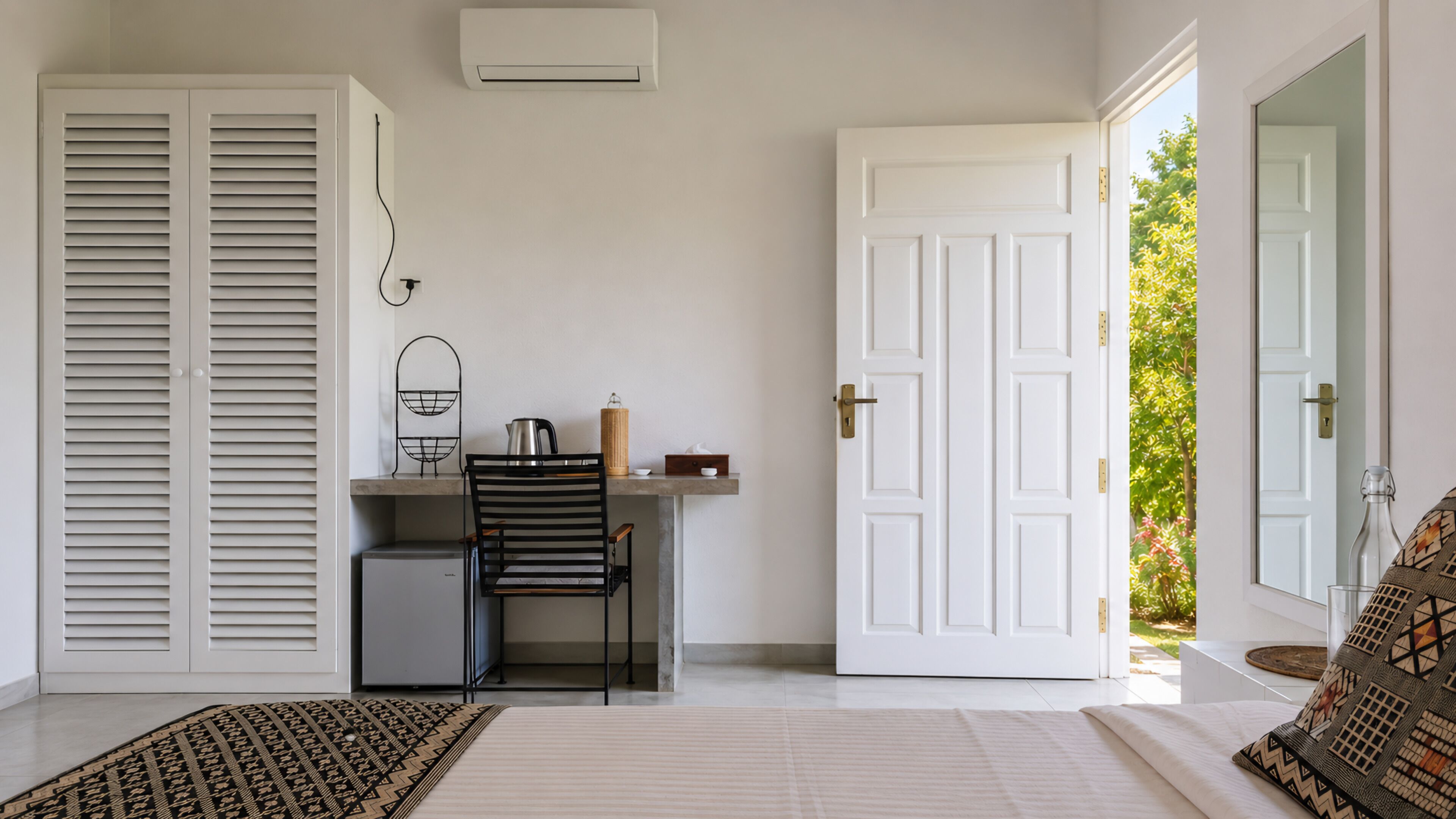 A bedroom with a bed, a desk with a chair, a wardrobe, and a door leading to a garden.