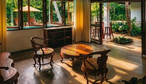 Una habitación con una mesa y sillas de madera, una ventana con vistas a zonas verdes y una pequeña piscina.