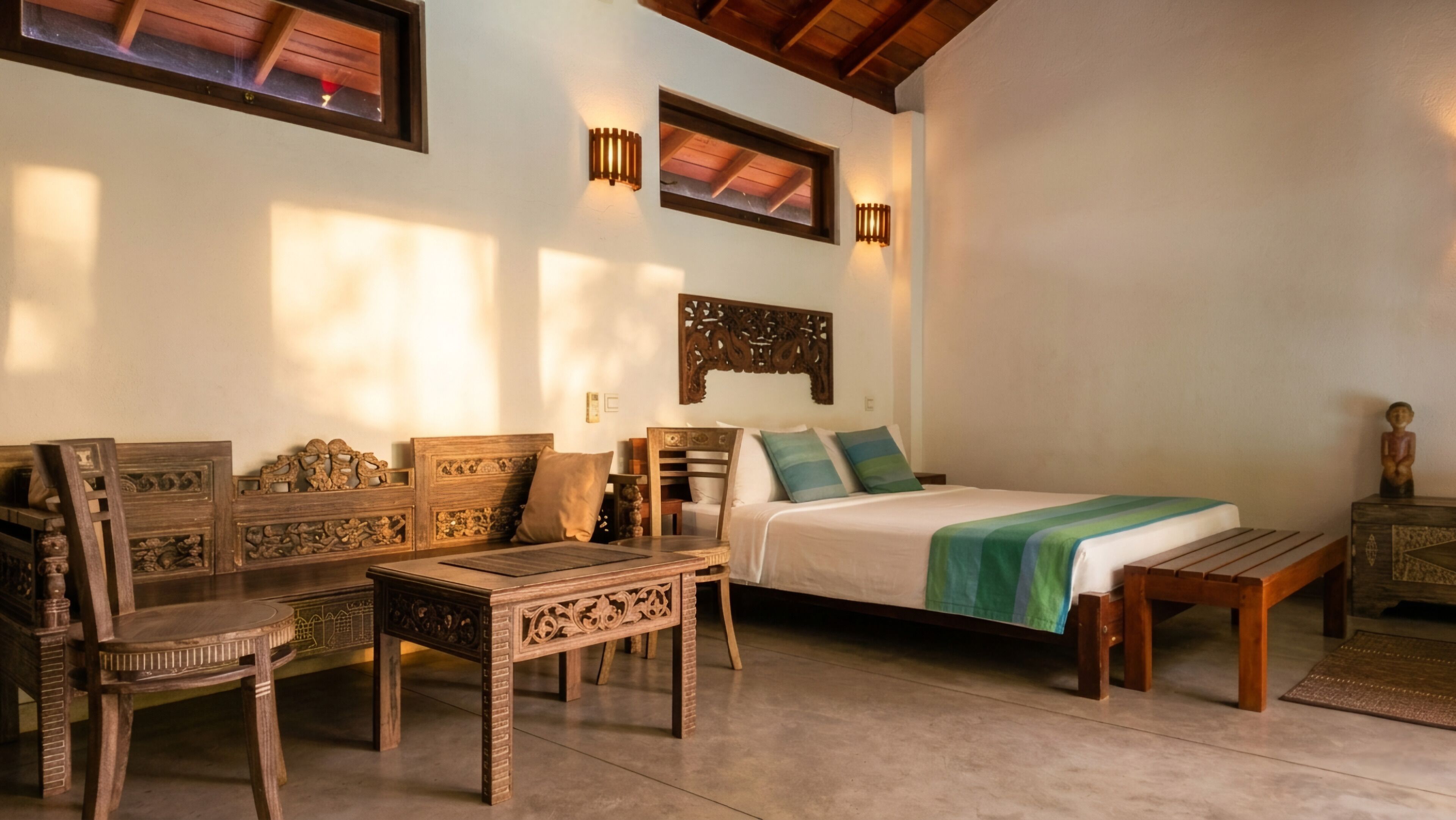 A room with a bed, a wooden sofa, a small table, and a decorative wall piece.