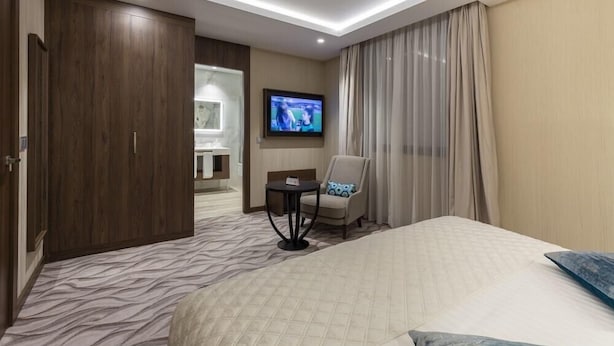 A hotel room with a bed, a chair, a TV, and a bathroom visible through an open door. - AZ Grand Oran Hotel (Es Senia)