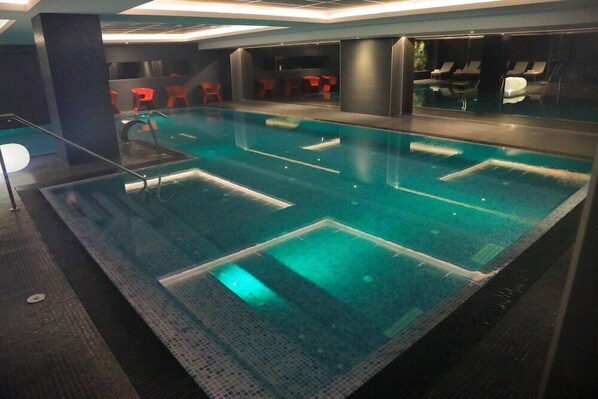 Una piscina con múltiples carriles y una zona de bar con sillas rojas.