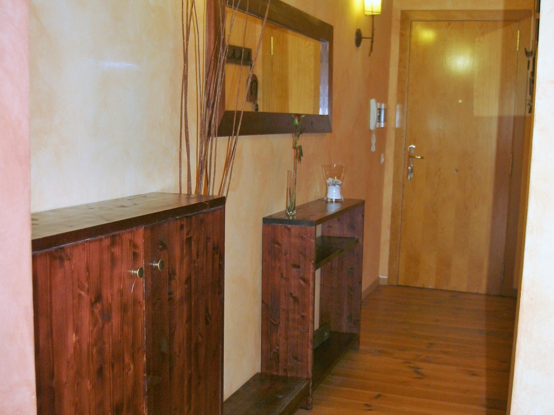 A wooden hallway with a mirror, a small table with a vase, and a door.