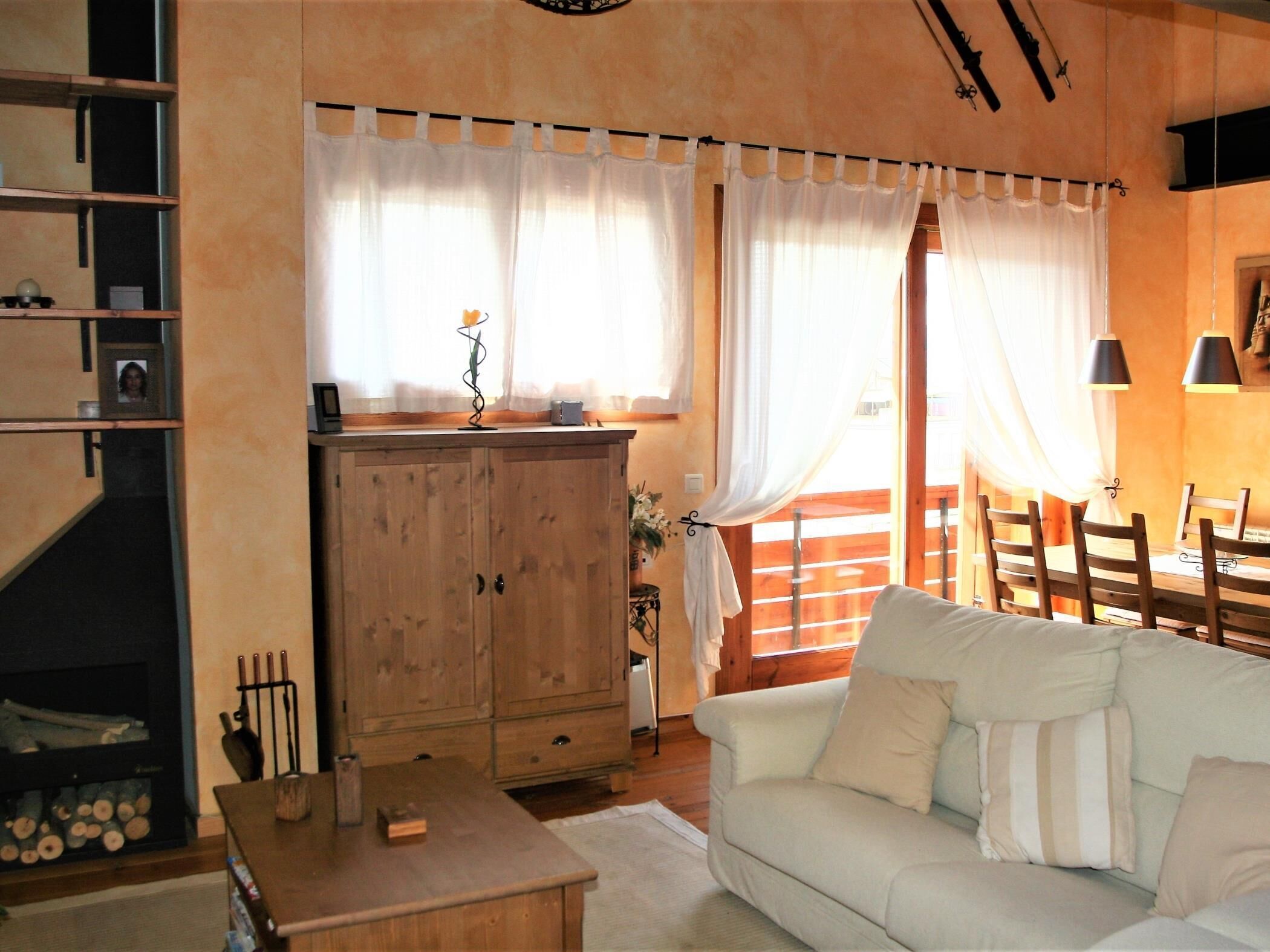 Una sala de estar acogedora con un aparador de madera, un sofá blanco y un comedor con sillas de madera.