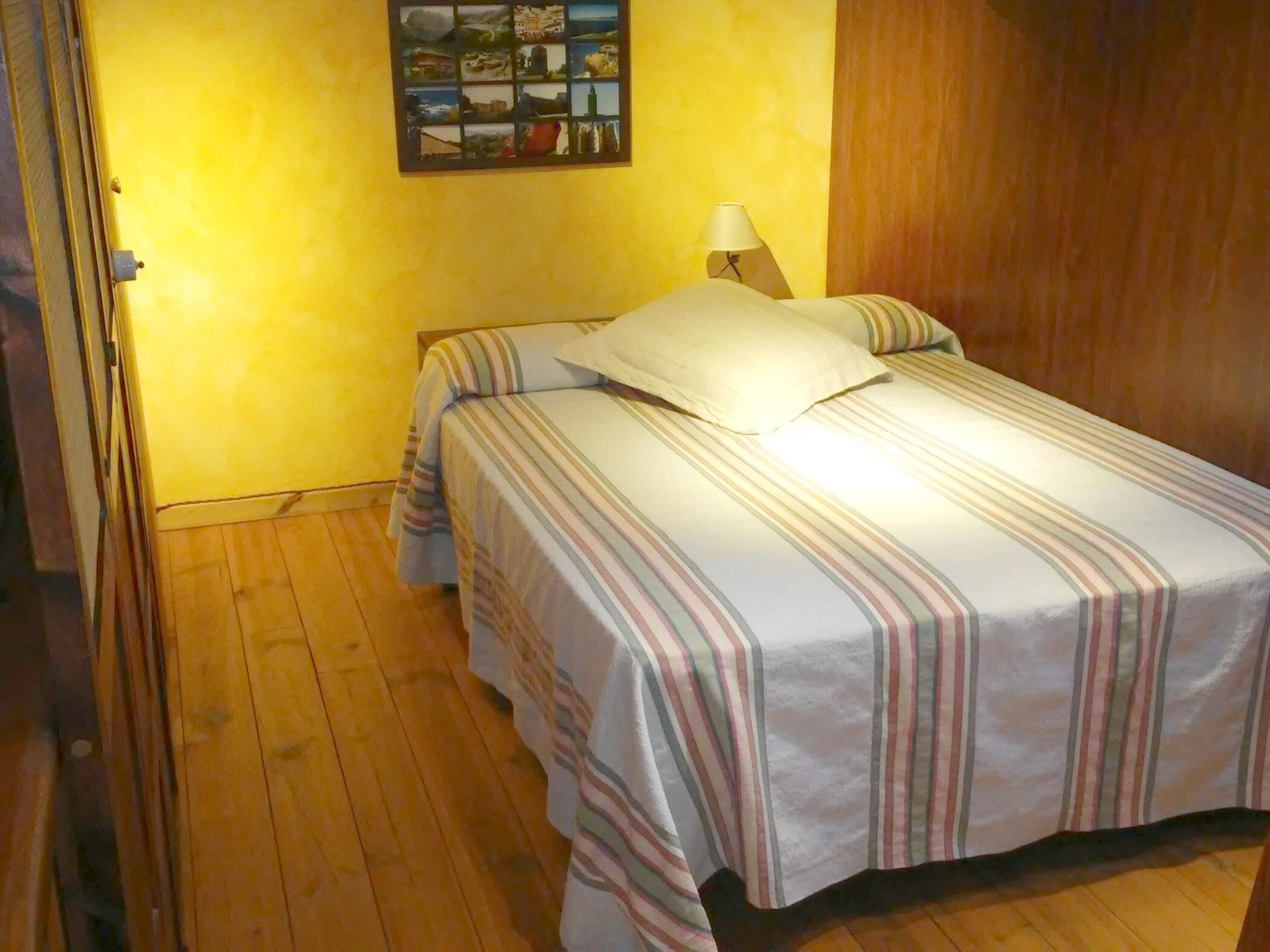 A room with a bed, a nightstand, a lamp, and a wall-mounted picture.