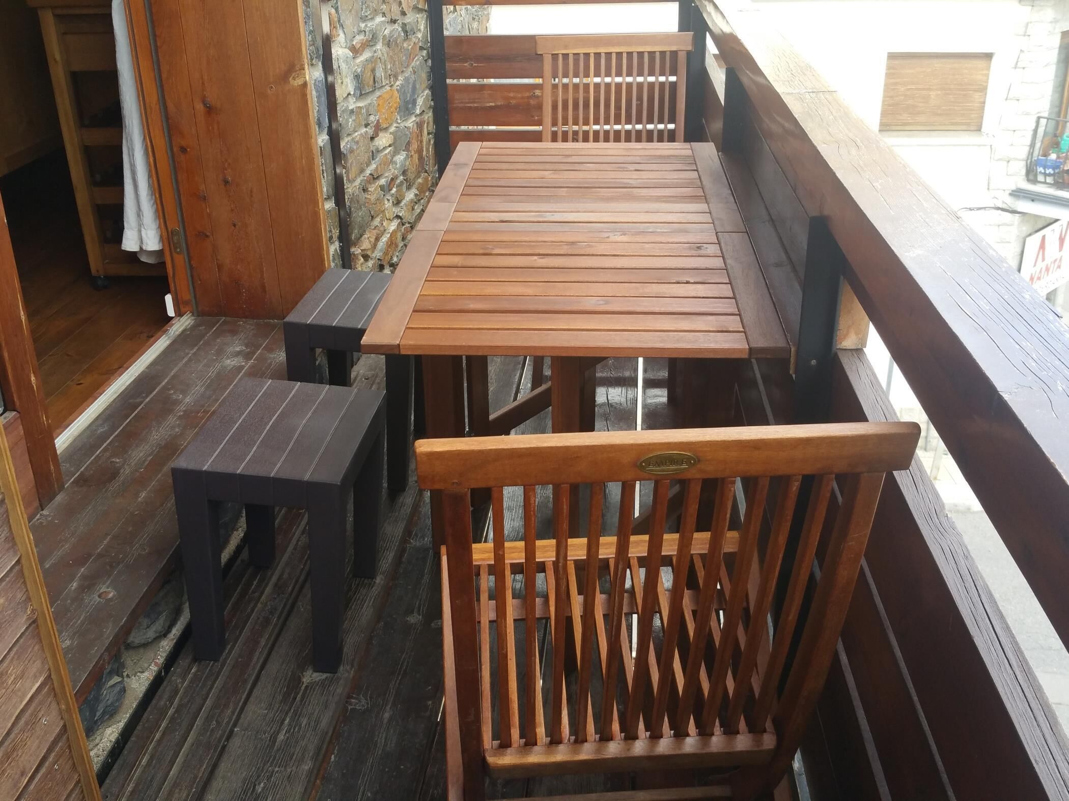 Een houten terras met een tafel, banken, een stenen muur en een houten leuning.