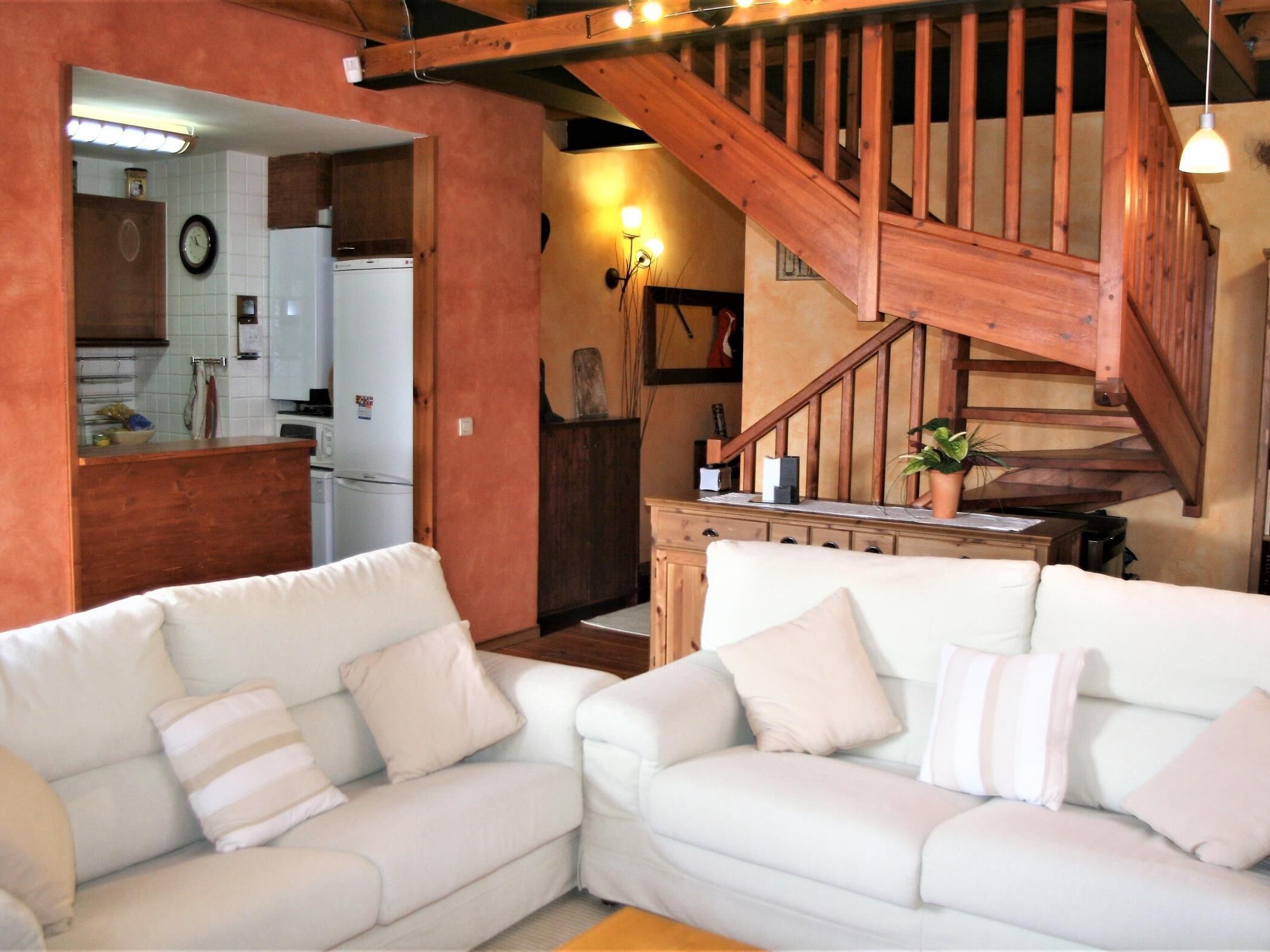 Ein Wohnzimmer mit weißen Sofas und einer Holztreppe.