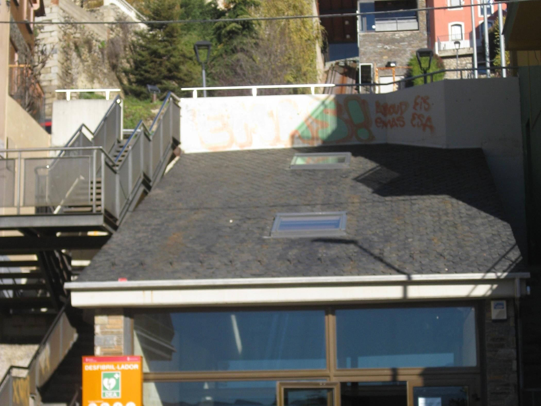 Een gebouw met een schuin dak, een zichtbaar raam en een bord met tekst.