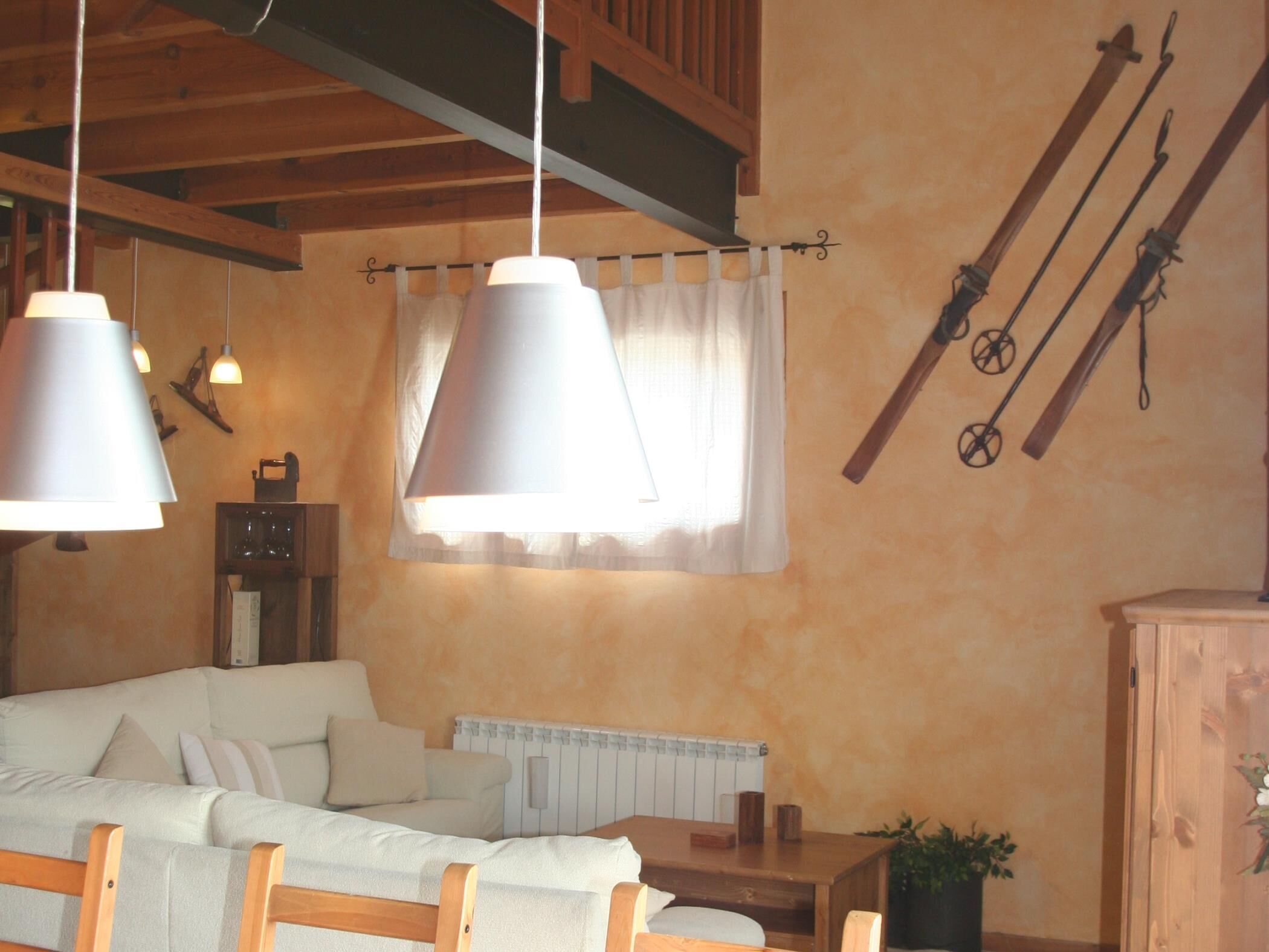 Una habitación acogedora con techo de madera, un sofá blanco, una mesa y un radiador.