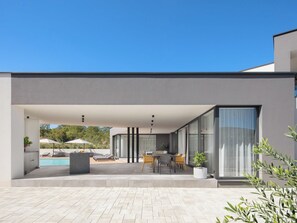 Een modern huis met een overdekte patio, een zwembad en een eethoek.