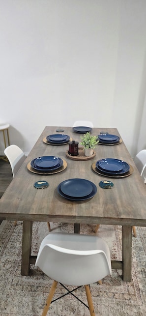 A rectangular dining table with a wooden finish, surrounded by white chairs with wooden legs. - Family-Friendly New Townhome in lovely Wayside community (Uhland)