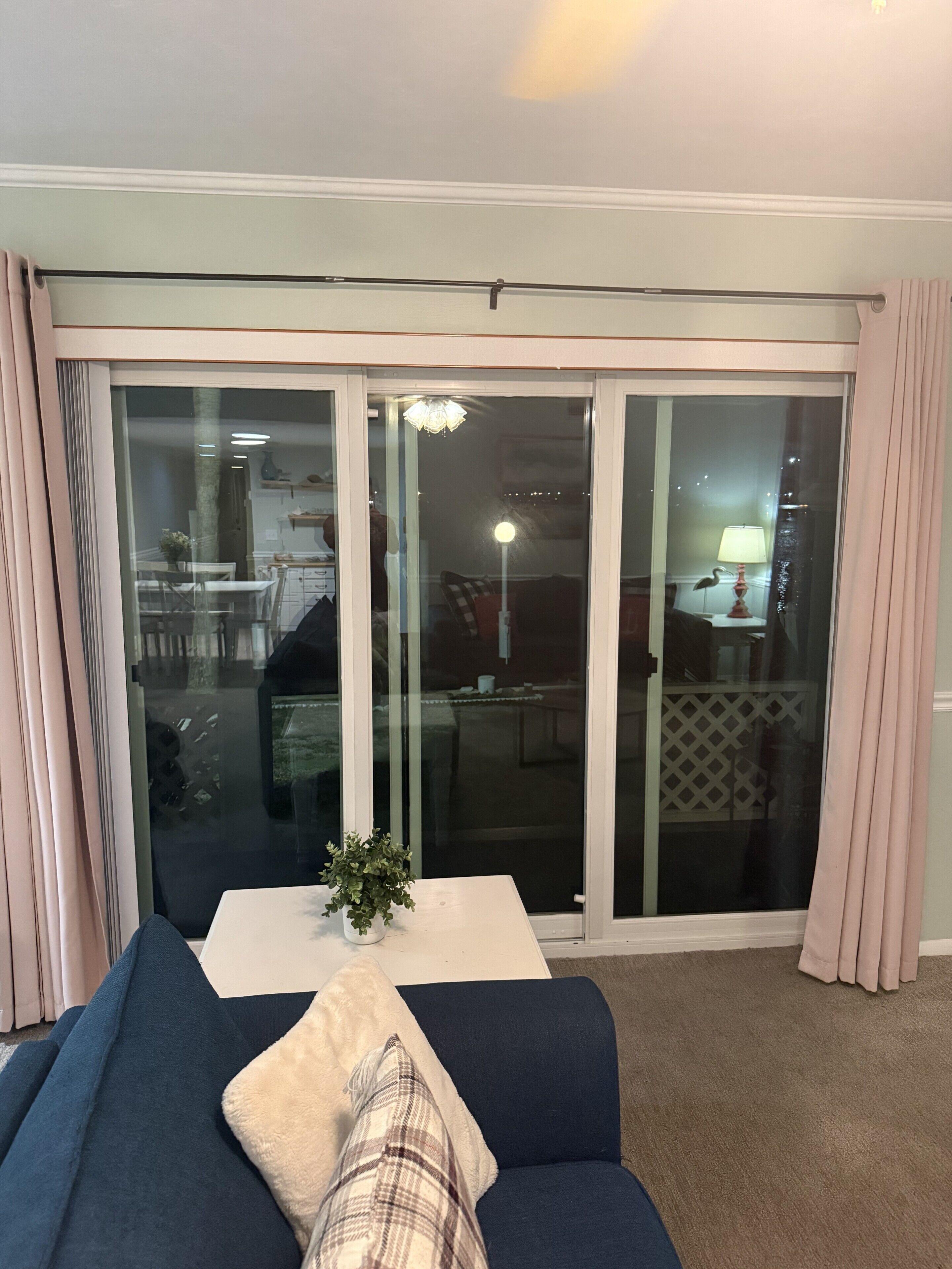 A living room with a sofa, a small table with a plant, and a sliding glass door leading to a balcony.