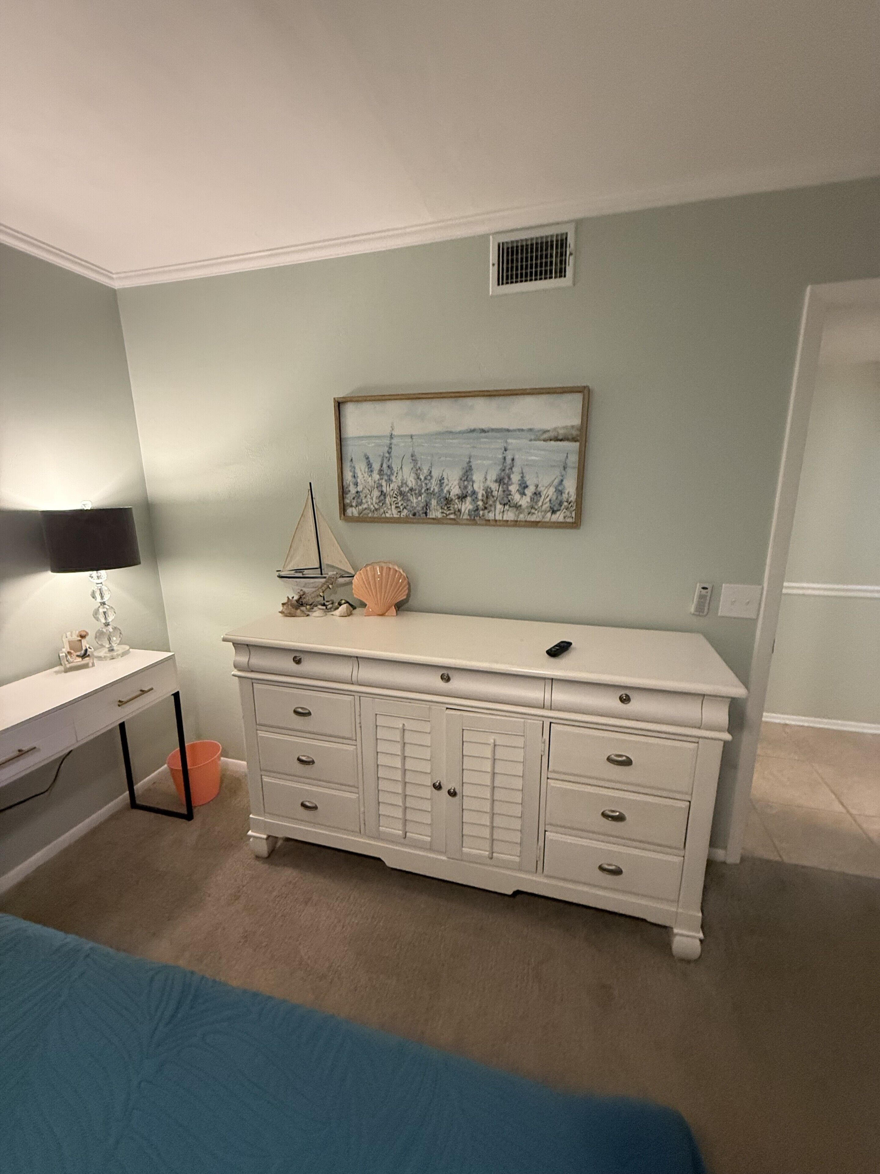 Un dormitorio con cama, cómoda, escritorio y un cuadro en la pared.
