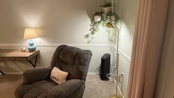 Una sala de estar con un sillón marrón, una lámpara de pie, una mesita con lámpara y una lámpara de pie alta con plantas.