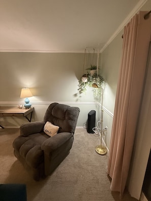A living room with a brown armchair, a floor lamp, a small table with a lamp, and a tall floor lamp with plants. - Daytona Riverfront Haven Retreat on the Halifax (Port Orange)