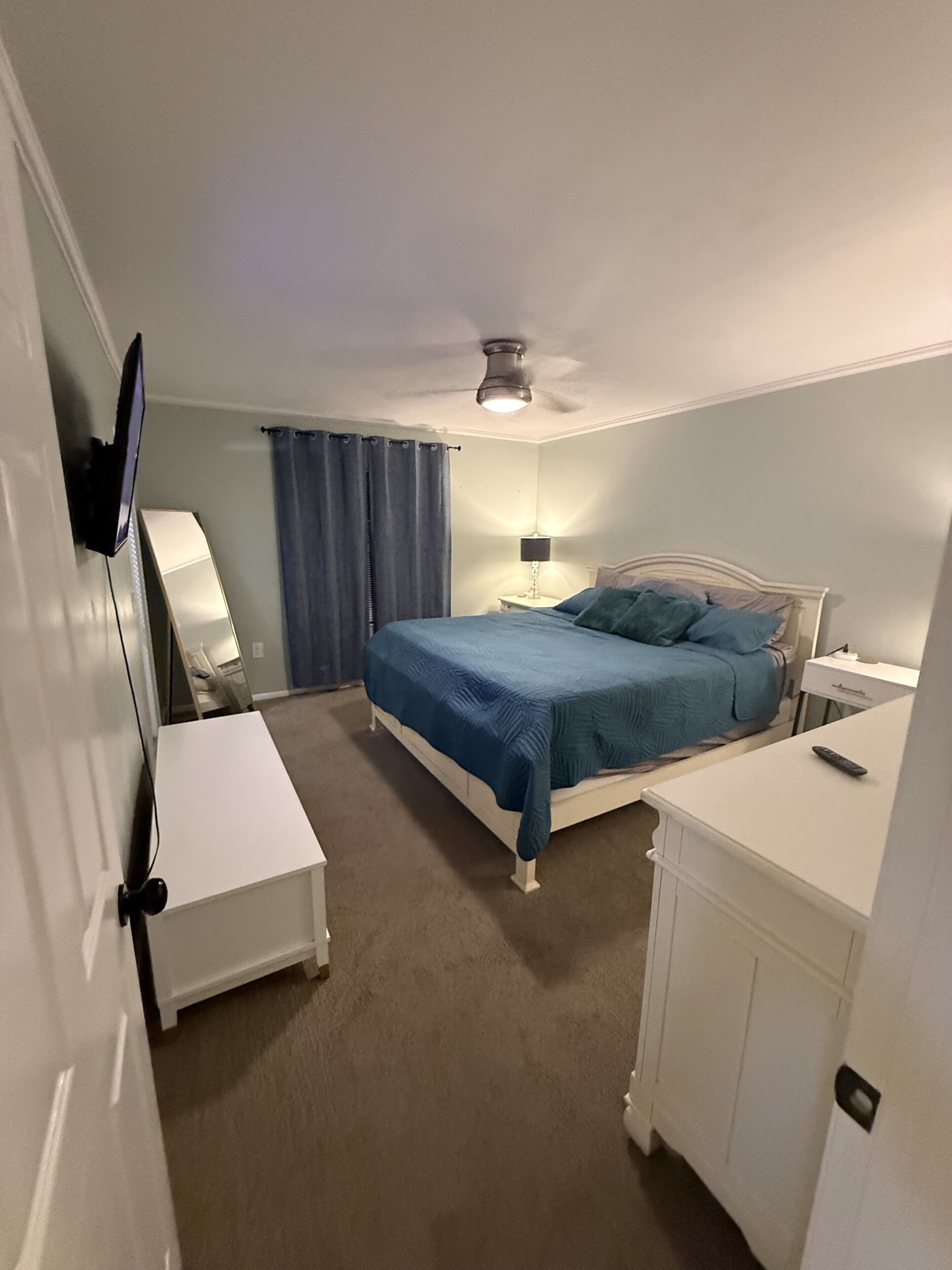 Ein Schlafzimmer mit Bett, Schreibtisch, Stuhl, Fernseher und Deckenventilator.