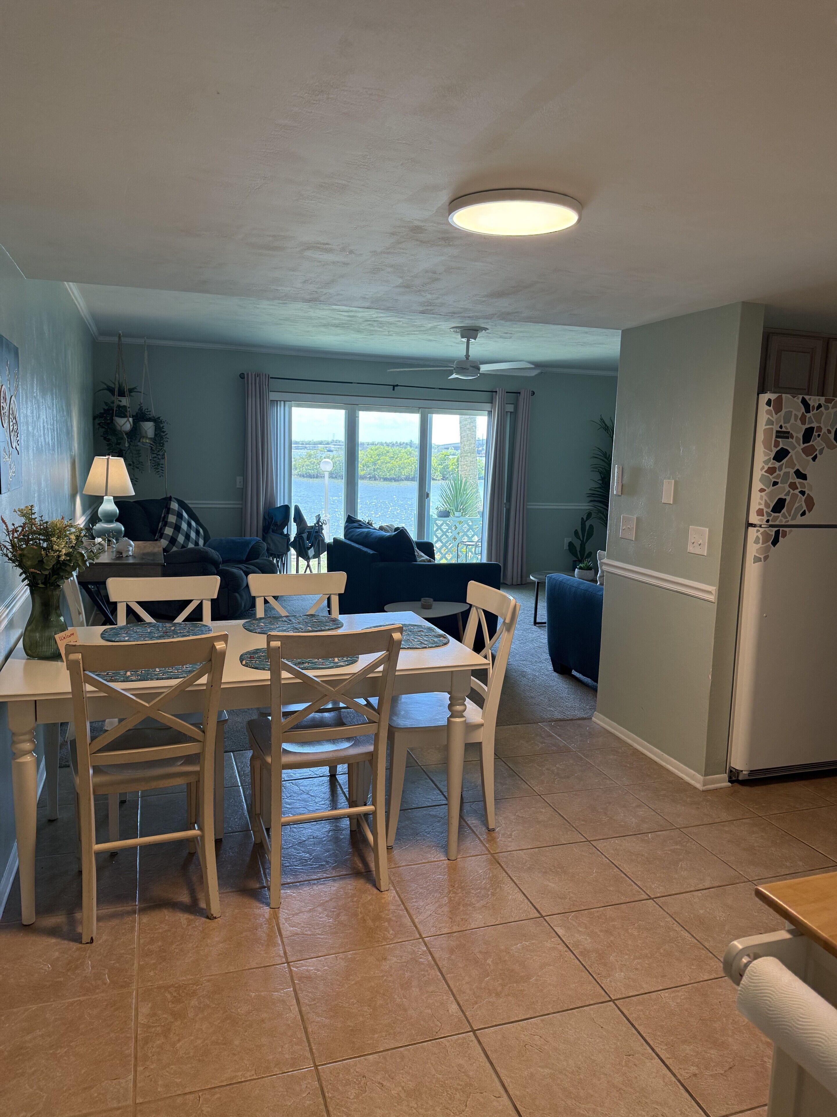 A dining area with a table and chairs, a ceiling fan, and a view through large windows.