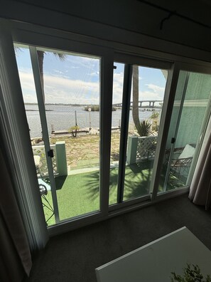 A room with a large sliding glass door leading to a balcony with a view of a body of water and a bridge. - Daytona Intercostal Retreat Home  3 Beds (Port Orange)