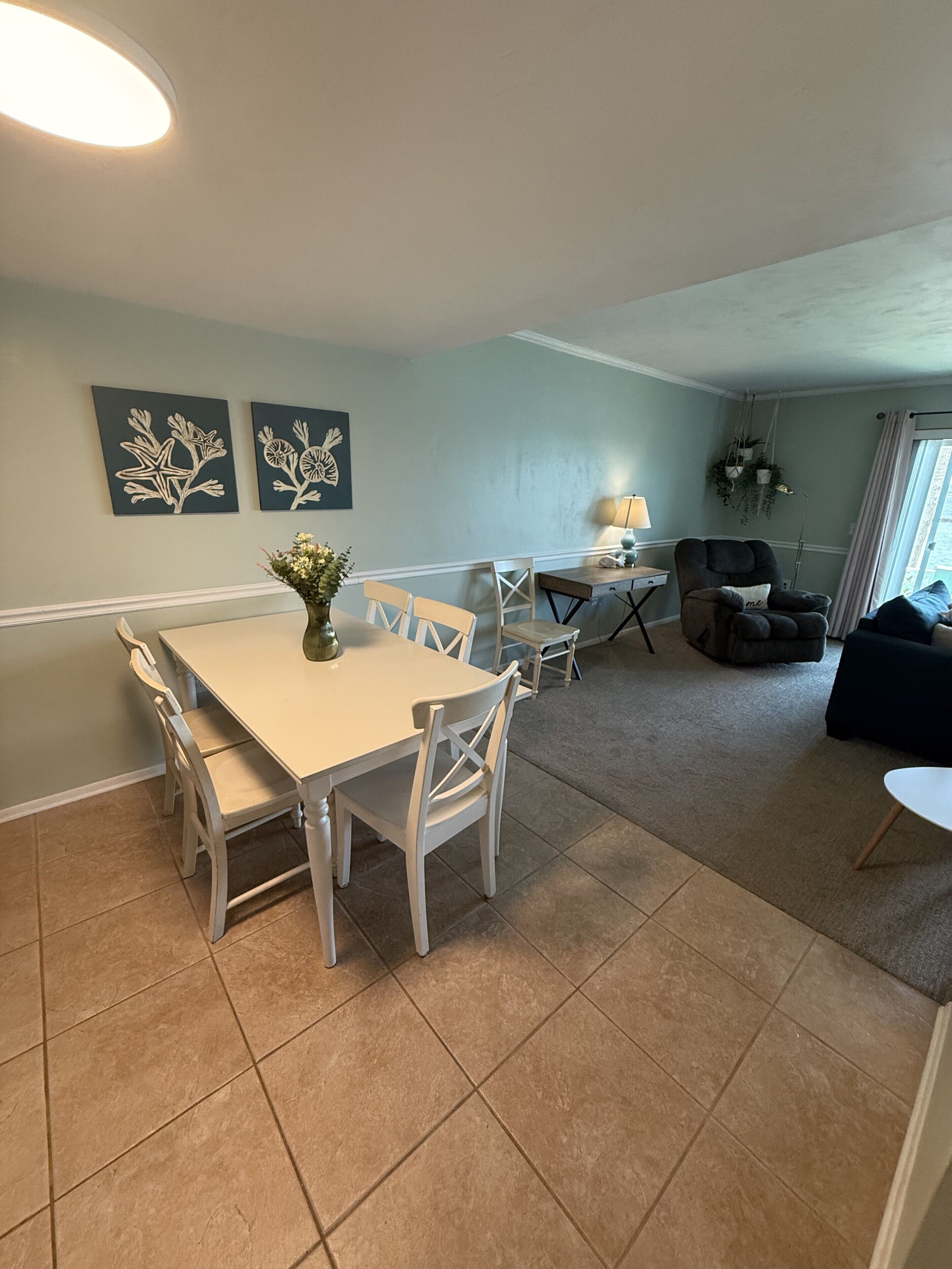 A dining area with a white table and chairs, a vase with flowers, and wall art.