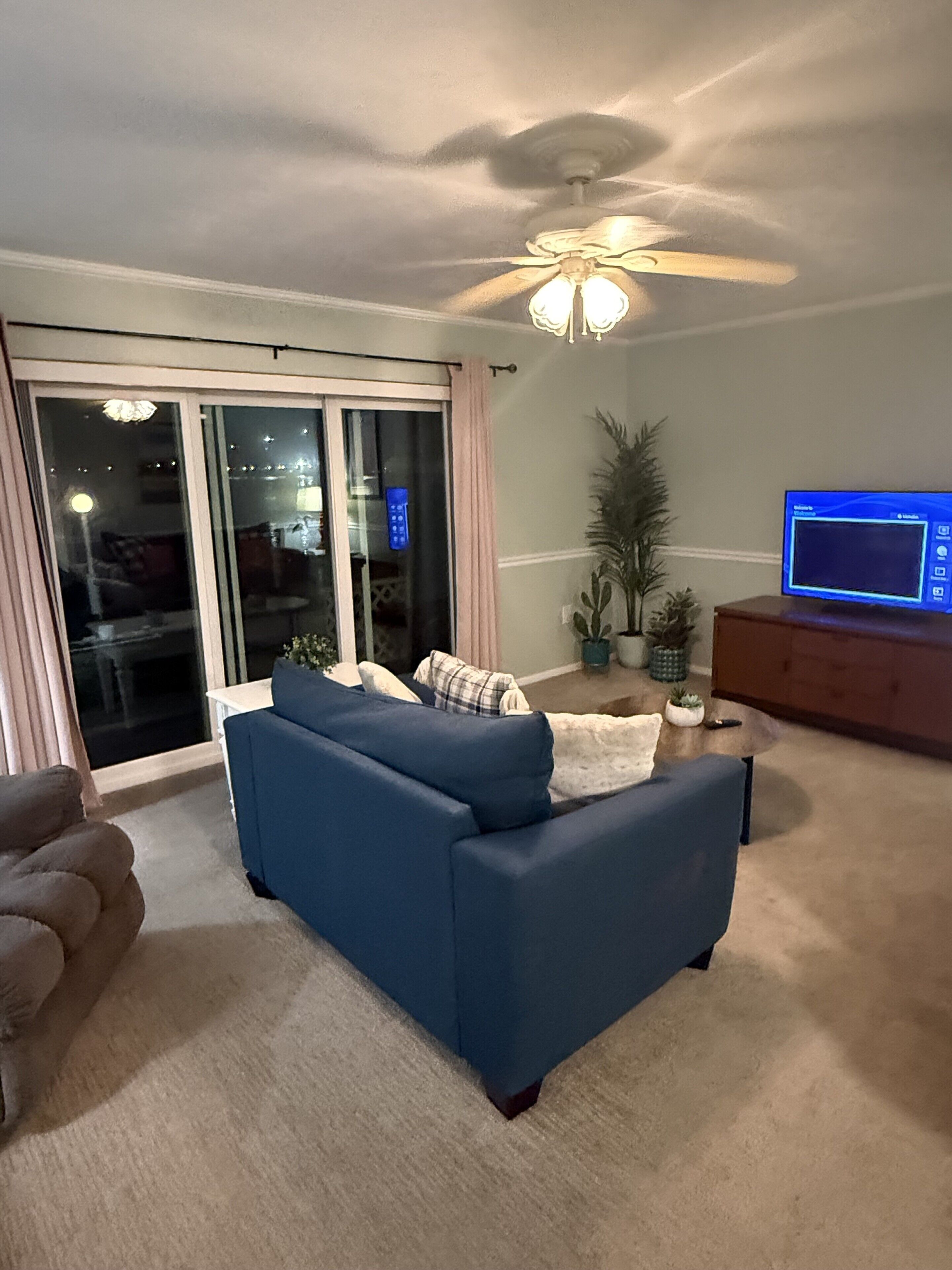 A living room with a blue sofa, a television on a wooden stand, and a ceiling fan.