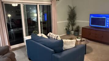 A living room with a blue sofa, a television on a wooden stand, and a ceiling fan.
