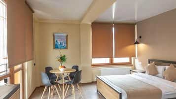 Una habitación de hotel con una cama, una mesa redonda con sillas, una ventana con persianas y un cartel en la pared.