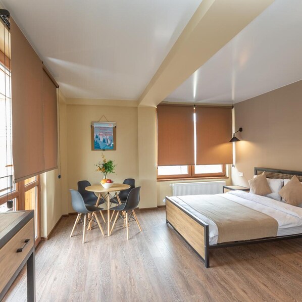 Una camera d'albergo con un letto, un tavolino rotondo con sedie, una finestra con persiane e un quadro appeso al muro.