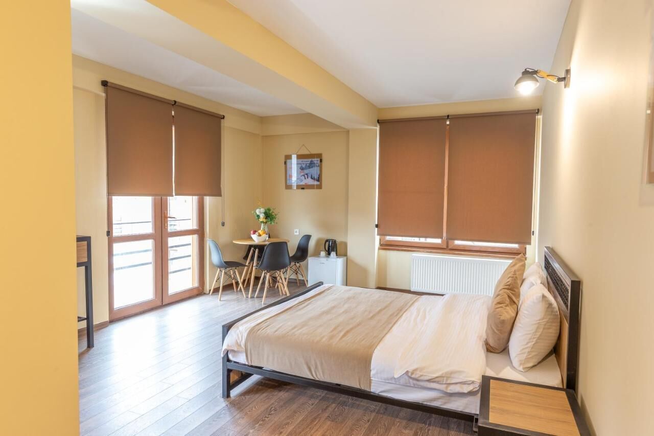 Un dormitorio con cama, escritorio y silla. Hay una ventana con persianas, un radiador y un cuadro en la pared.